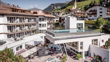 A modern hotel with a rooftop infinity pool, outdoor seating, and a scenic mountain backdrop.