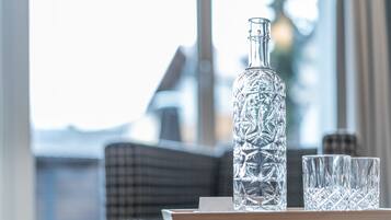 A clear glass bottle and two glasses on a table with a checkered cushion in the background.