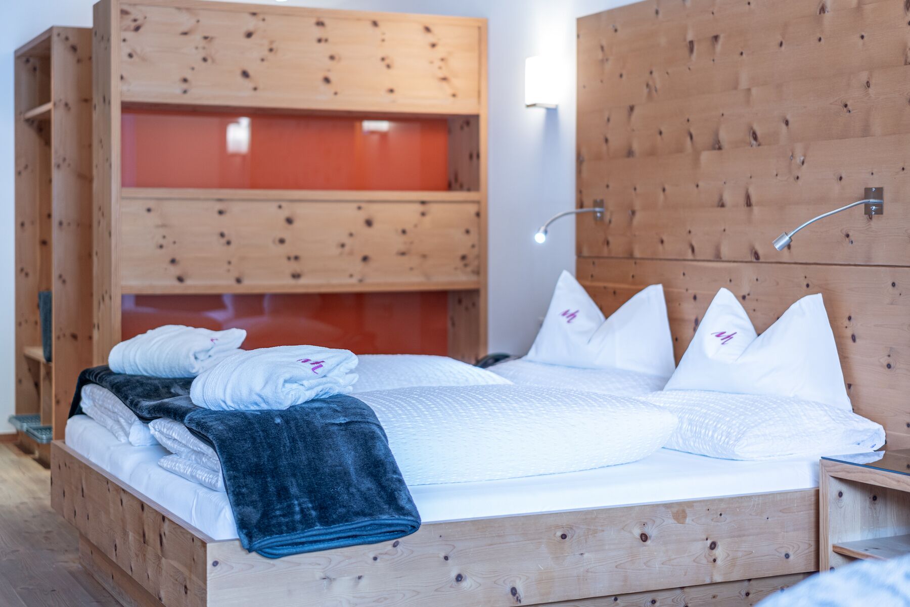 A wooden bed with white bedding and pillows, a blue blanket, and a wooden wardrobe with a red panel.