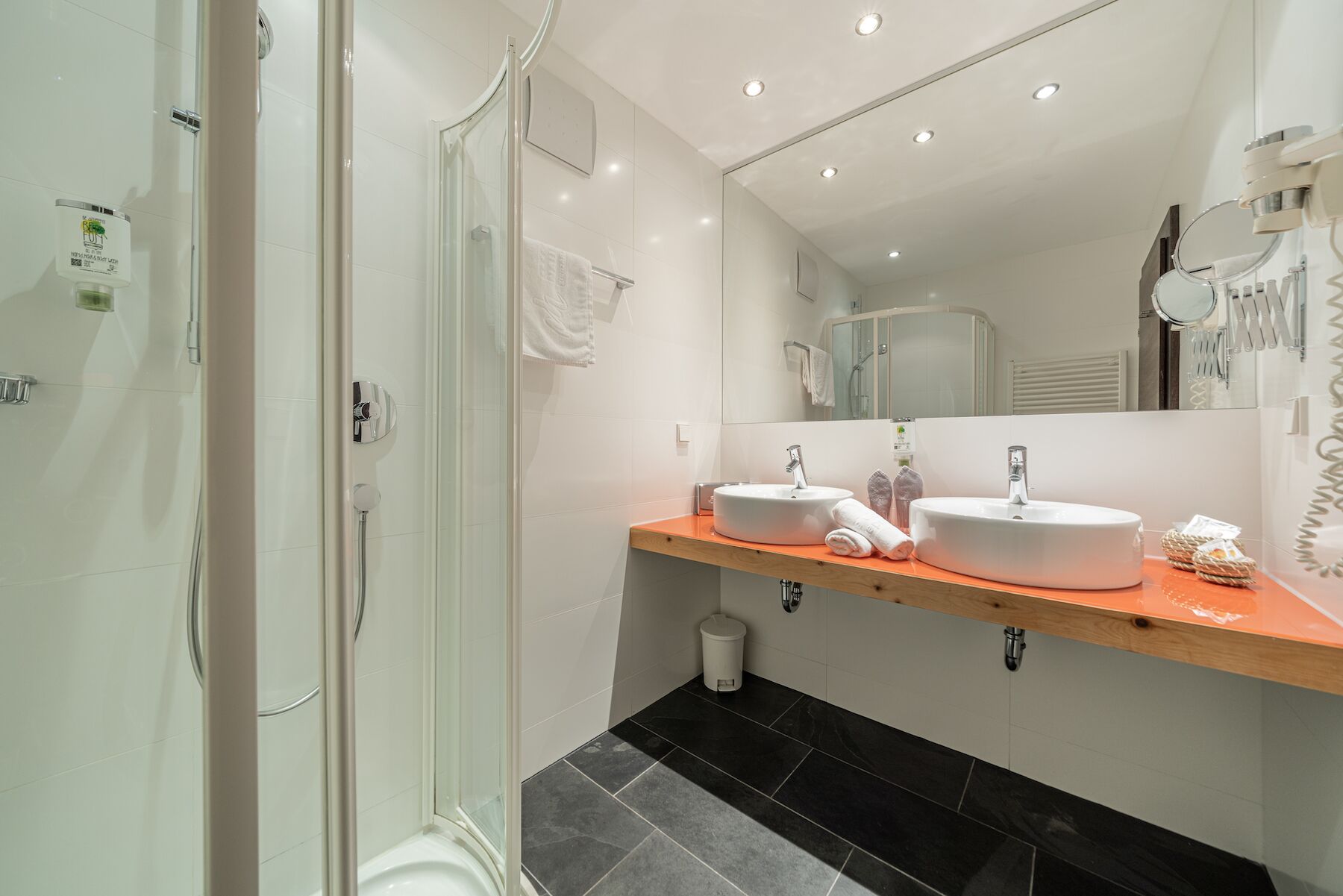 Un baño moderno con cabina de ducha de vidrio, dos lavamanos y un mueble de tocador de madera.
