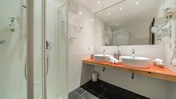 Un baño moderno con cabina de ducha de vidrio, dos lavamanos y un mueble de tocador de madera.