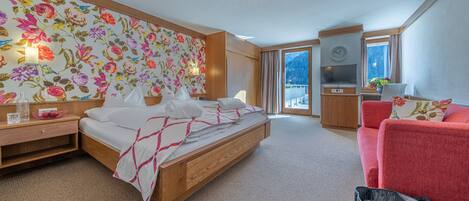 Habitación de hotel con una cama grande, un sofá rojo, un armario de madera, un televisor y un balcón con vistas a la montaña.