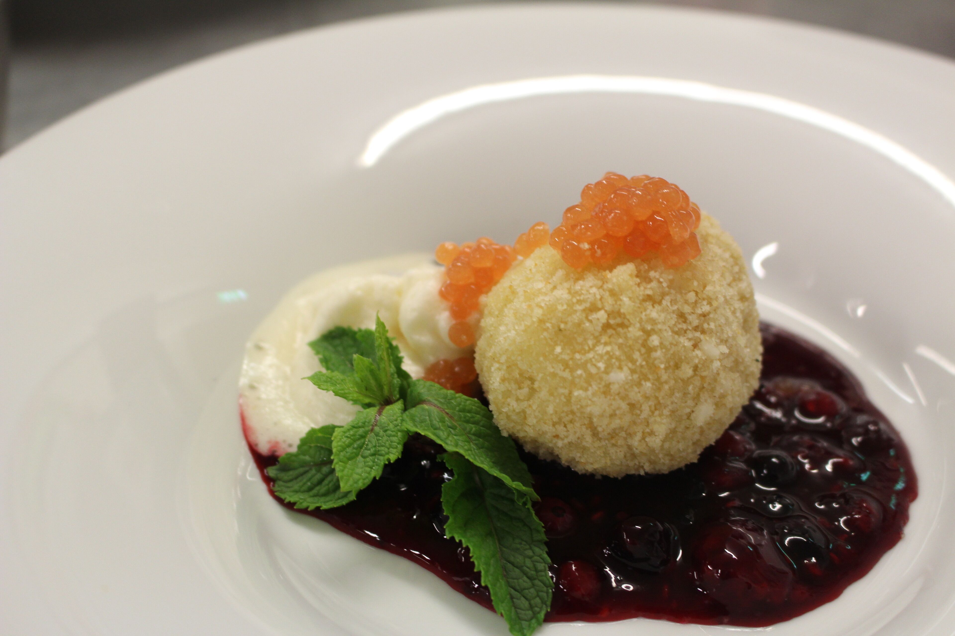 A dessert with a round, crumbly base, a scoop of ice cream, and a berry compote on a white plate.