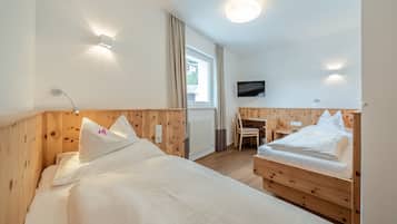 A room with two beds, a desk, a chair, a TV, and a window with curtains.