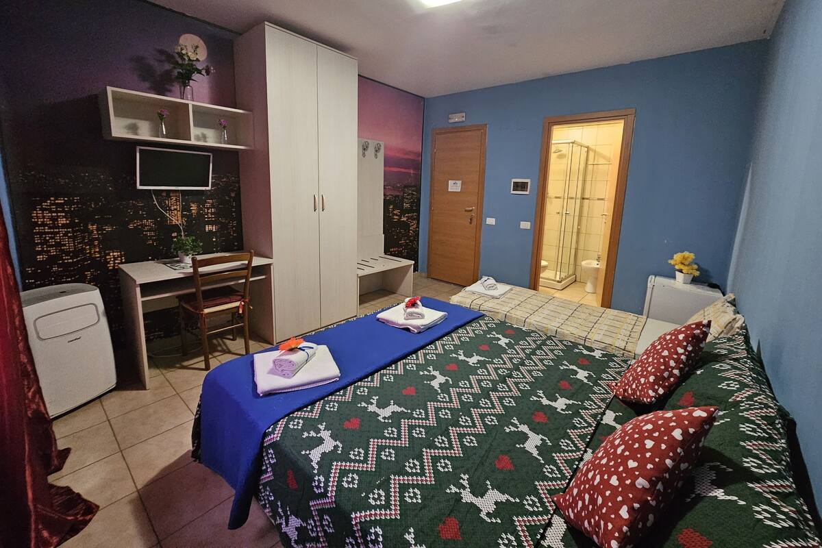 A bedroom with a bed, a desk, a wardrobe, and a shower area.