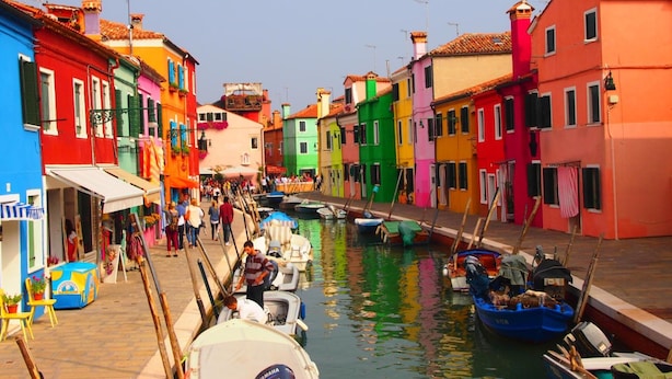 A canal lined with colorful buildings, boats docked along the water, and people walking by. - Ca’ Dei Fiori 1 Venezia (Mestre)