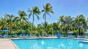 A swimming pool with lounge chairs and umbrellas, surrounded by palm trees. - Catch the Day, Toast the Night- Fish, Dive & Island Vibes! (Tavernier)