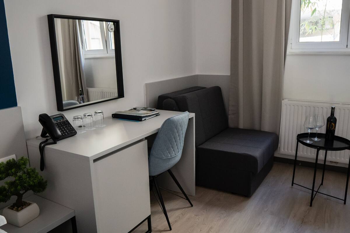 A compact hotel room with a desk, chair, and a small seating area.