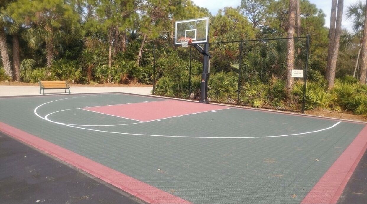 An outdoor basketball court with a bench and trees in the background.
