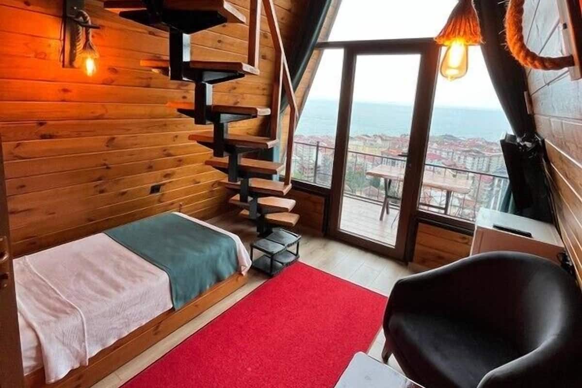 Een gezellig chalet met houten inrichting, een bed, een rood kleed, een tafel en uitzicht op het landschap door een groot raam.
