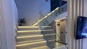A modern staircase with glass railings and illuminated steps, leading to a room with a television and a potted plant. - Loya Butik Otel - Bungalow (Çayeli)
