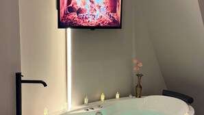 A modern bathroom with a freestanding bathtub, a mounted television, and a vase with flowers. - Loya Butik Otel - Bungalow (Çayeli)
