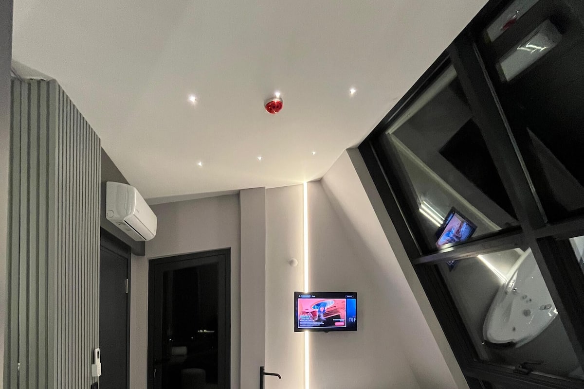 Een moderne badkamer met een badkuip, toilet en douchegedeelte. Er is een televisie aan de muur bevestigd.