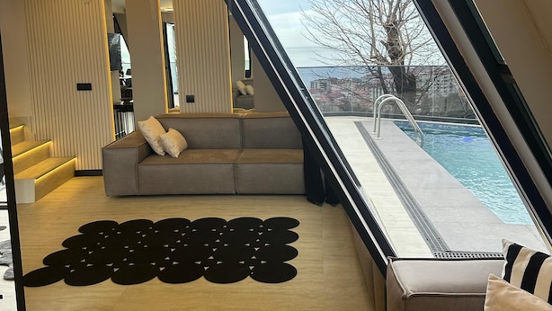 A modern interior with a sofa, a patterned rug, and a view of a swimming pool. - Loya Butik Otel - Bungalow (Çayeli)