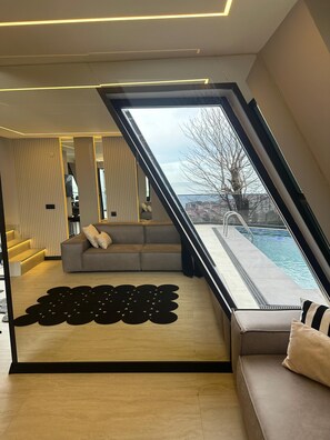 A modern interior with a sofa, a patterned rug, and a view of a swimming pool. - Loya Butik Otel - Bungalow (Çayeli)