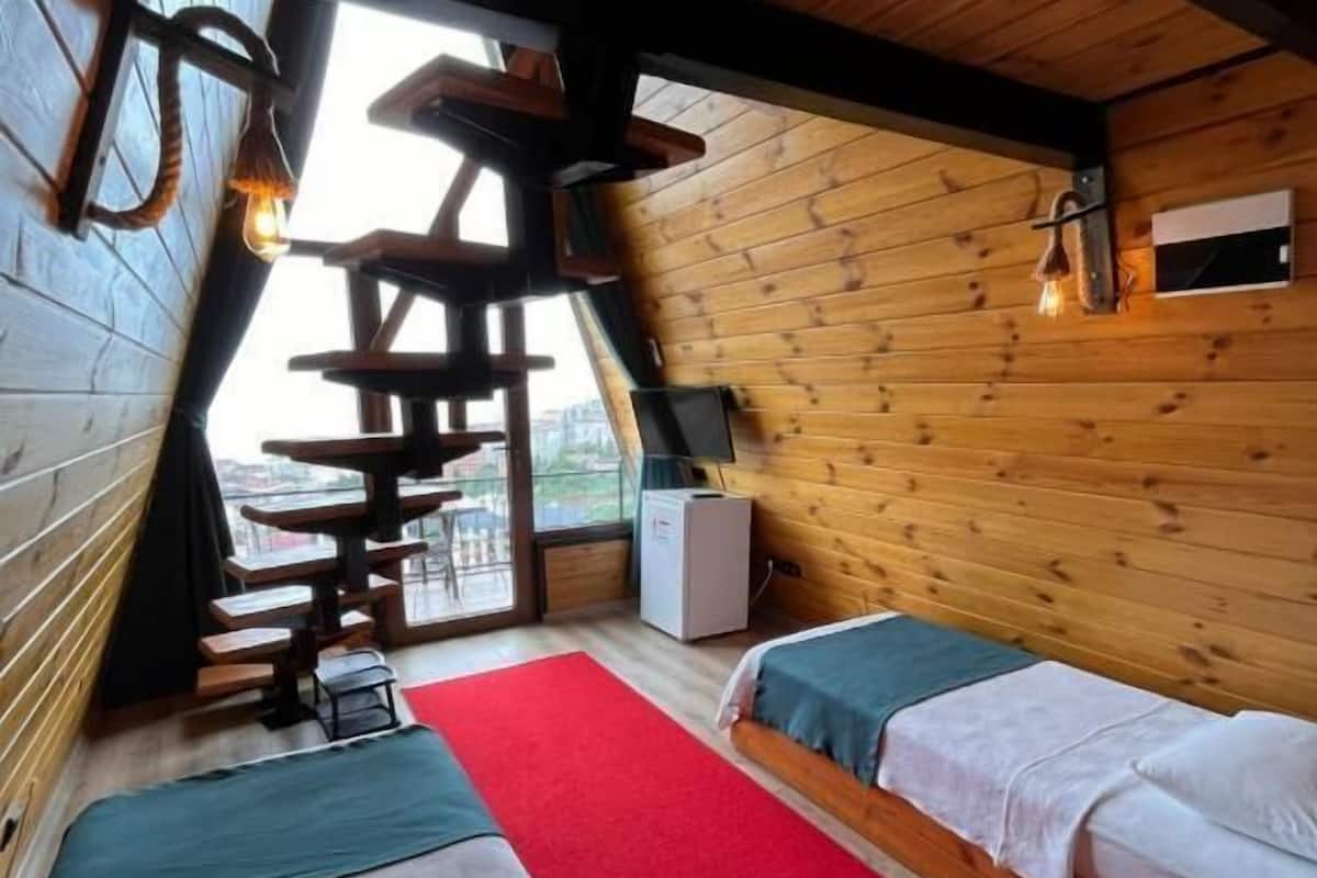 Een gezellig vakantiehuisje met schuine wanden, houten muren, een rood tapijt en een klein bureau met een lamp.