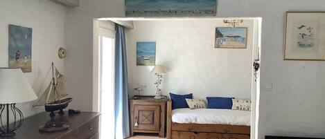 A bedroom with a bed, a desk, a chair, a lamp, and a painting on the wall.