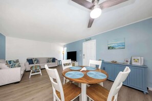 A living room with a dining table, white chairs, a ceiling fan, and a blue wall.