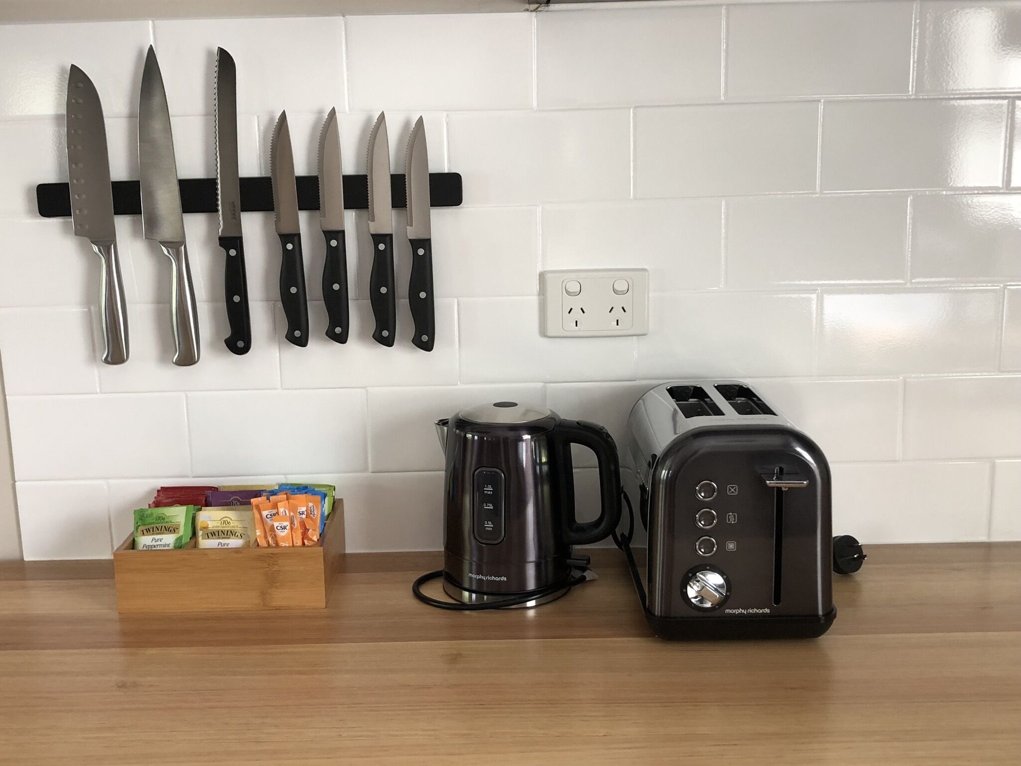 Una cocina con un colgador para cuchillos, una cafetera, un tostador y una caja de té Twinings.