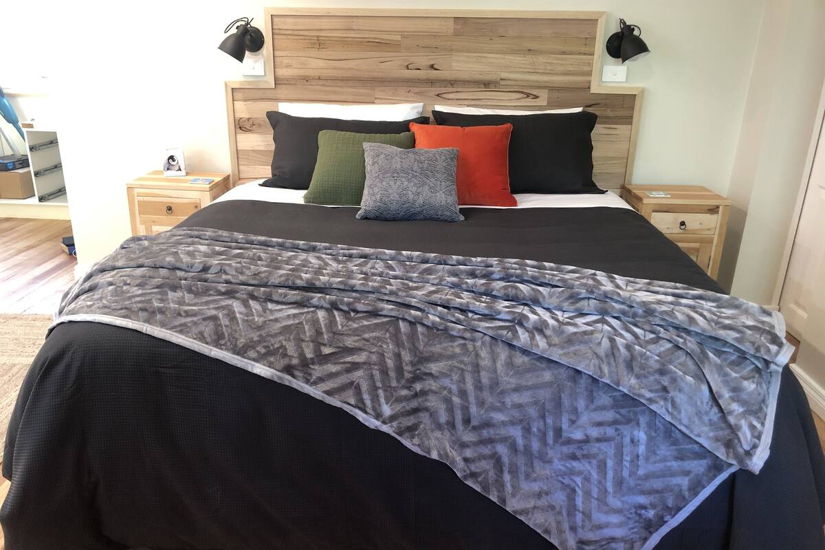 A neatly made bed with a patterned blanket, multiple pillows in various colors, and a wooden headboard.