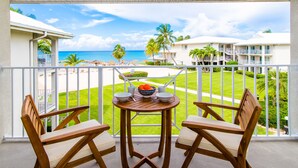 Ein Balkon mit zwei Holzstühlen und einem Tisch, der Blick auf einen Strand und Hotelgebäude bietet.