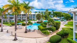 Ein Resort mit mehreren Swimmingpools, Palmen und einer gepflegten Rasenfläche.