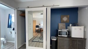 Ein kompakter Wohnbereich mit einer Schiebetür zu einem Schlafzimmer, einer Küchenzeile mit Mikrowelle und kleinem Kühlschrank sowie einer blauen Wand mit Dekoration zum Thema Kompass.