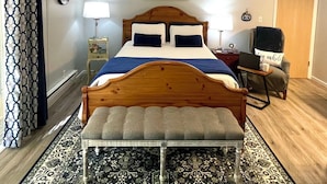 Ein Schlafzimmer mit einem Holzbett, zwei Nachttischlampen, einer Weltkarte an der Wand, einem Deckenventilator, einem gemusterten Teppich und einer Bank.