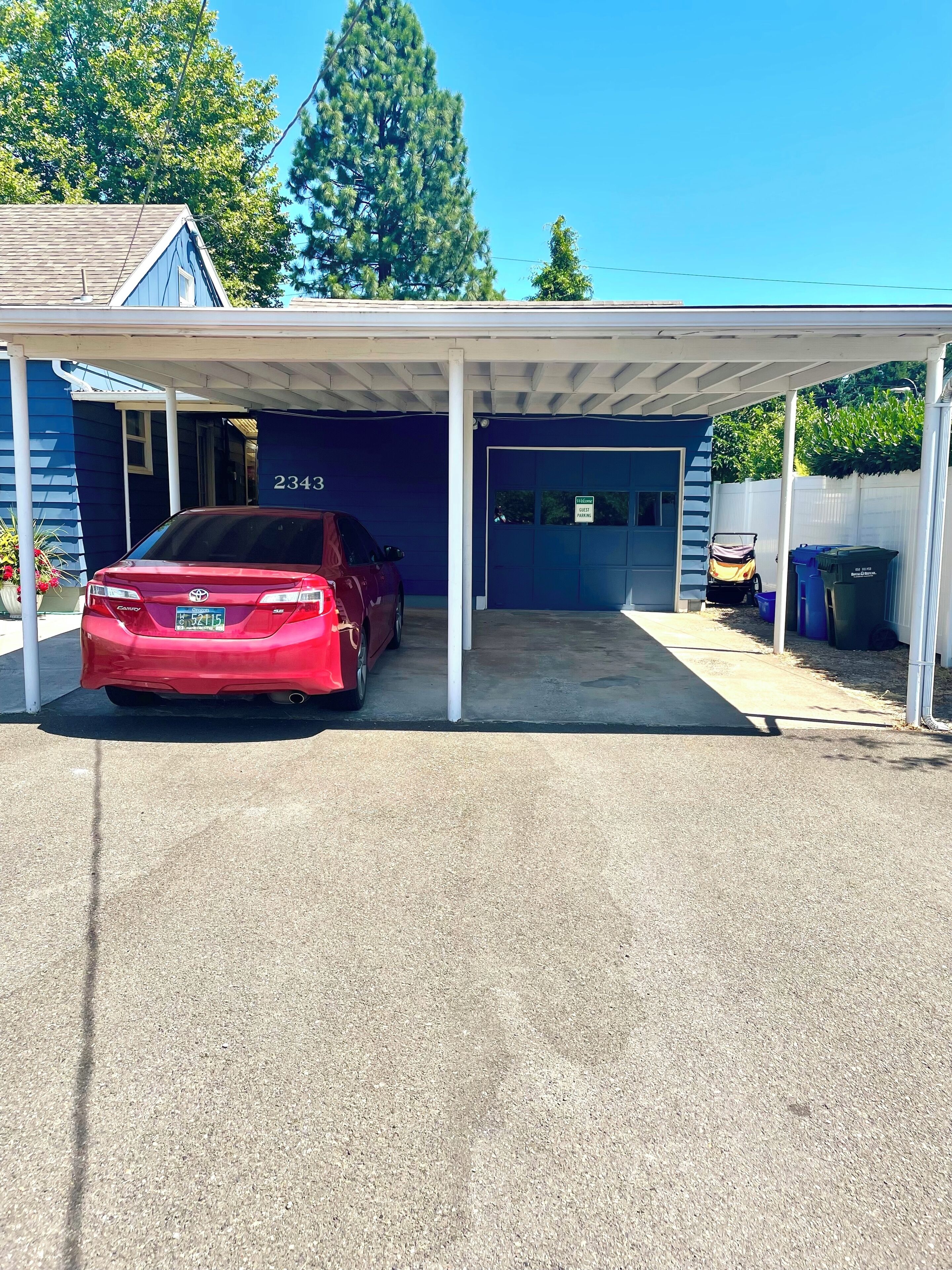 A red car parked in a covered garage with a blue building in the background.