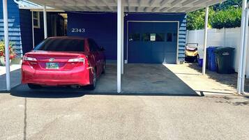 A red car parked in a covered garage with a blue building in the background.