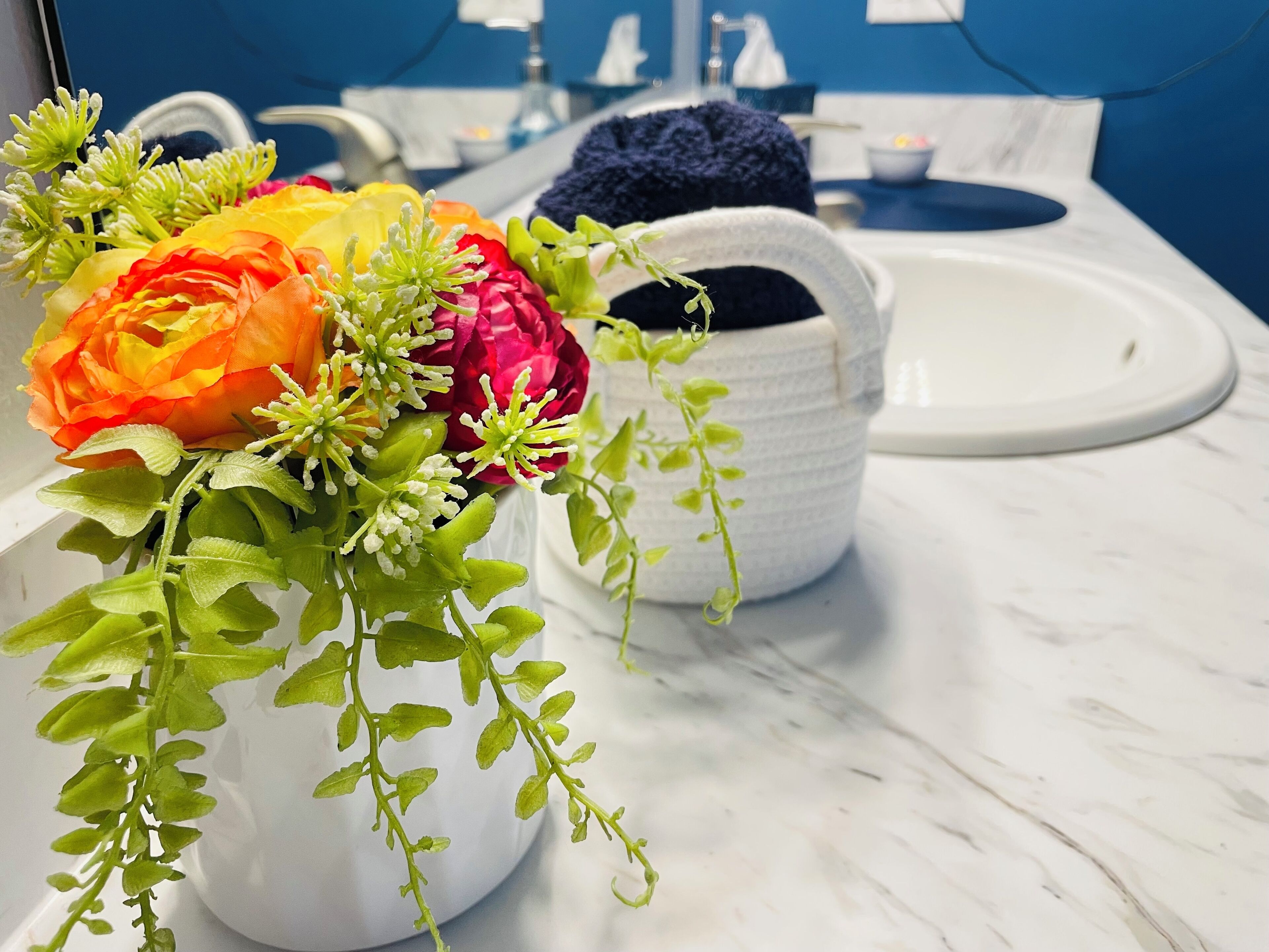 Ein Badezimmer mit einem weißen Waschbecken, einer weißen Vase mit Blumen und einem blauen Handtuch.