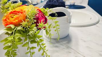 Ein Badezimmer mit einem weißen Waschbecken, einer weißen Vase mit Blumen und einem blauen Handtuch.