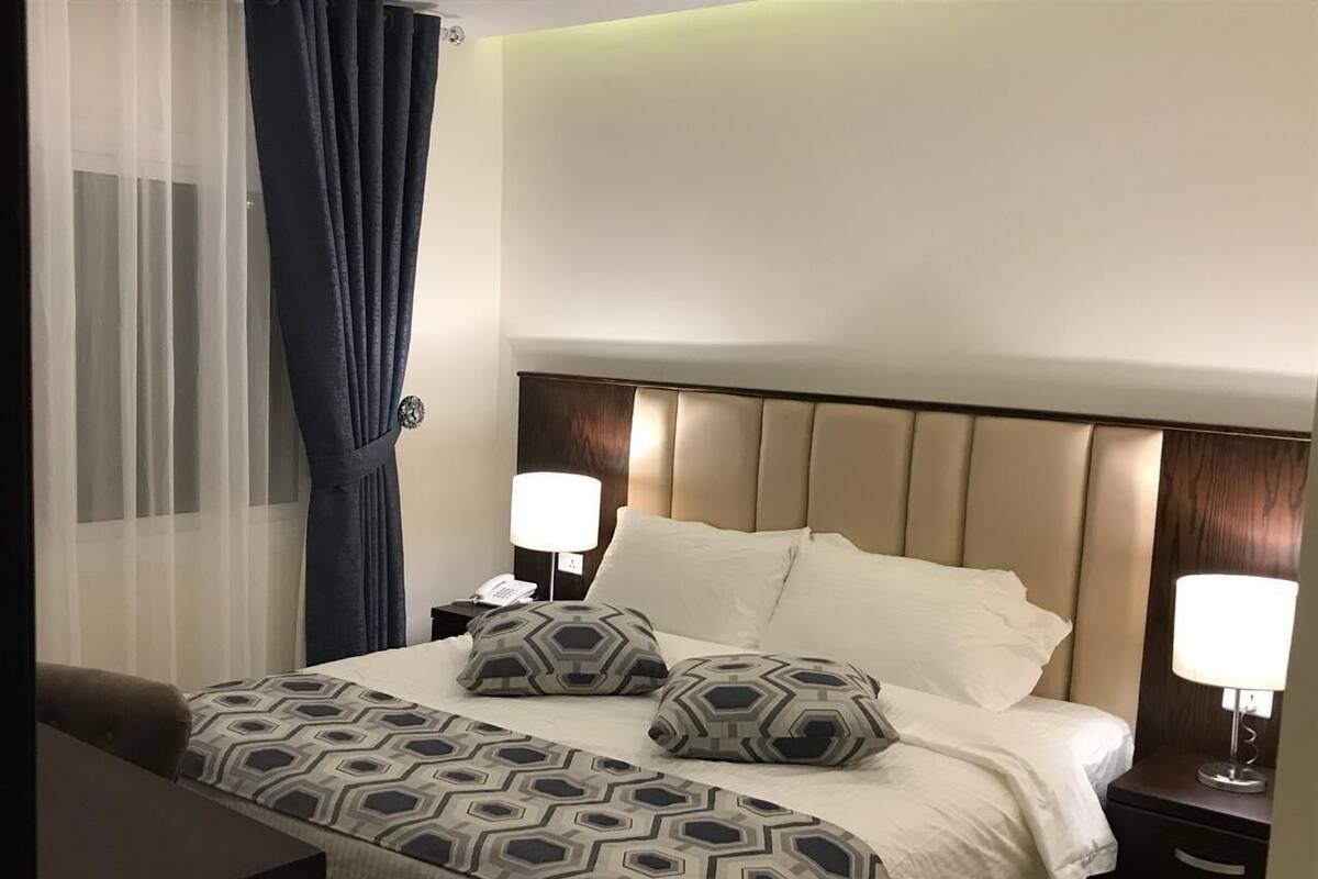 A hotel room with a bed, two bedside tables, a lamp, and a curtain.