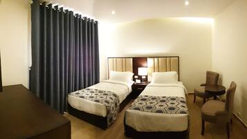 Habitación de hotel con dos camas, un escritorio, una silla y un ventanal con cortinas.