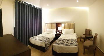 Habitación de hotel con dos camas, un escritorio, una silla y un ventanal con cortinas.