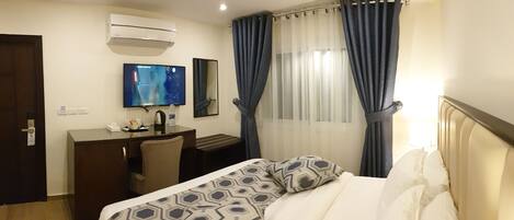 Une chambre d’hôtel comprenant un lit, un bureau avec une chaise, une télévision et un appareil de climatisation.