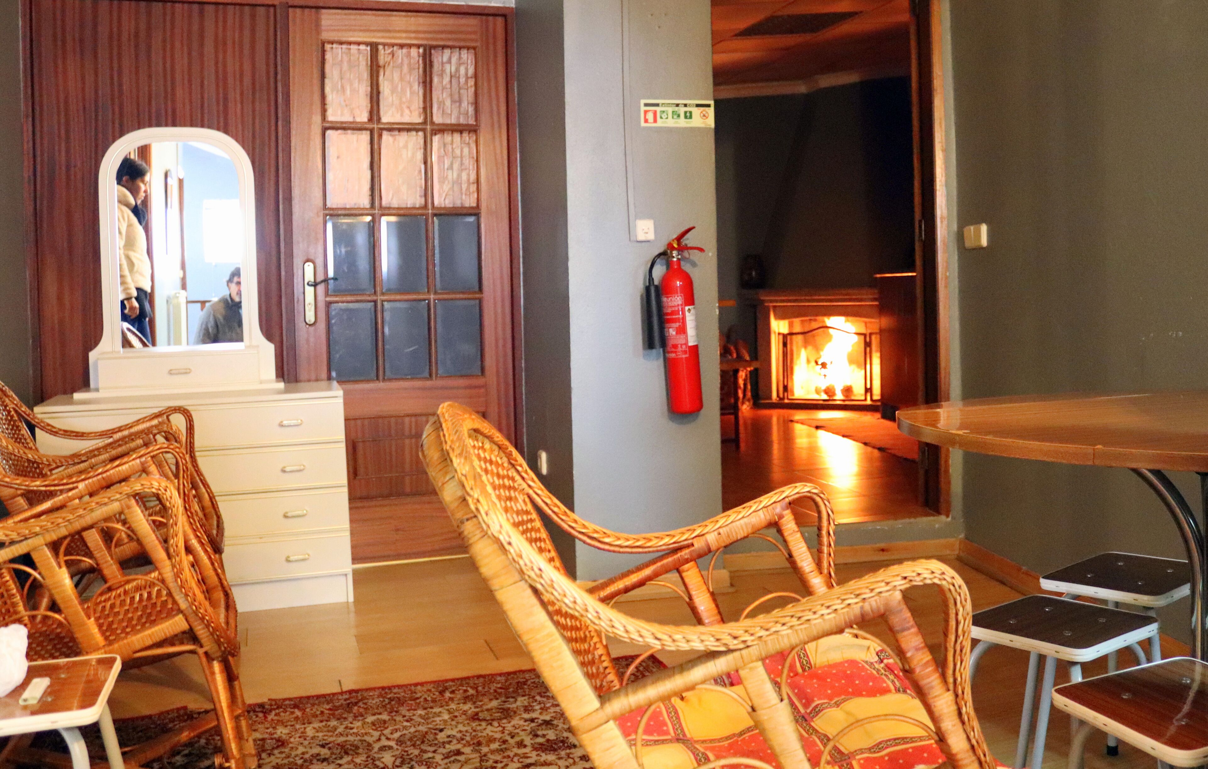 A room with wicker furniture, a white dresser, a mirror, a fire extinguisher, and a fireplace.