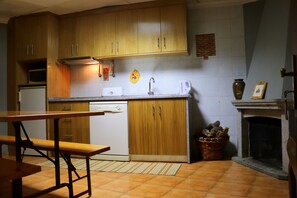 A compact kitchen with wooden cabinets, a built-in dishwasher, a sink, and a fireplace. - Alojamentos Estrela Peles (Seia)