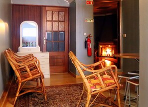 A room with wicker chairs, a wooden door, a fire extinguisher, and a fireplace. - Alojamentos Estrela Peles (Seia)