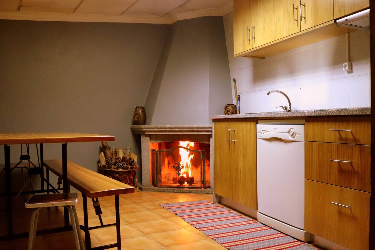 Uma cozinha com lareira, armários de madeira, bancada e um banco.