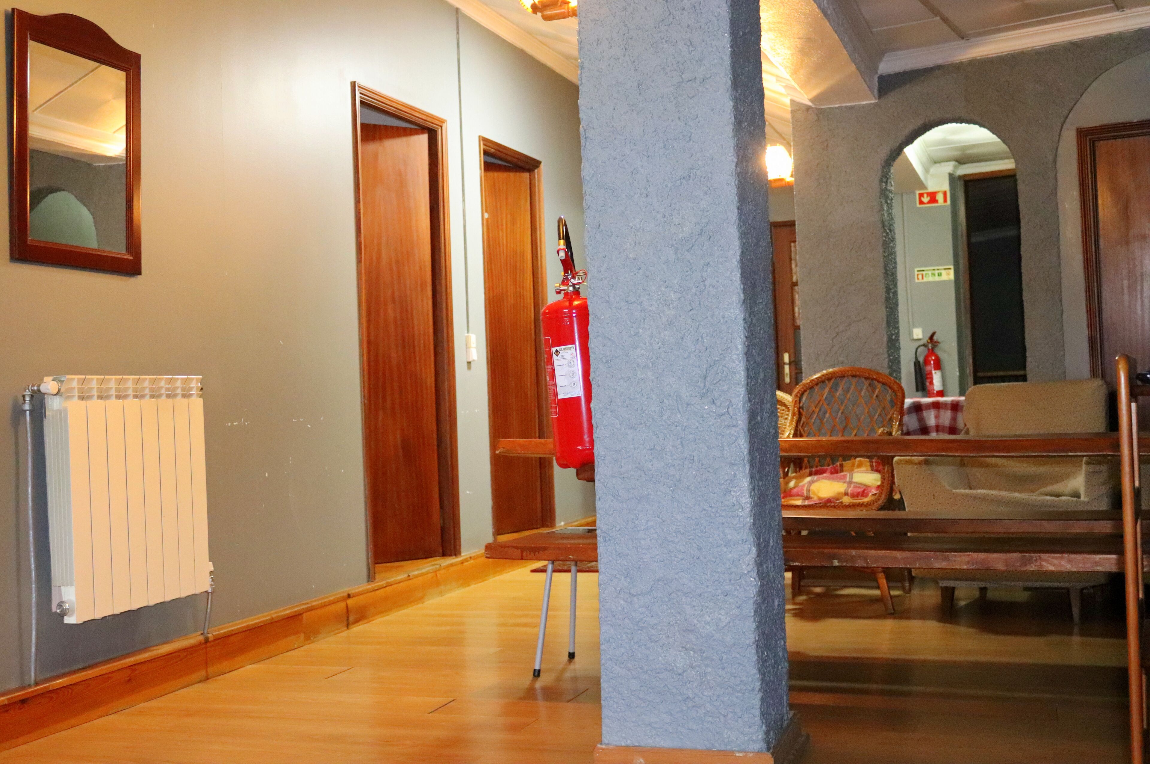 A hallway with wooden doors, a fire extinguisher, a radiator, and a dining area with chairs and a table.