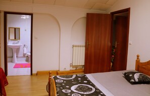 A bedroom with a bed, a wooden door, a bathroom with a sink and mirror, and a radiator. - Alojamentos Estrela Peles (Seia)
