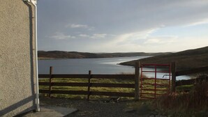 A view of a lake from a building with a gravel path leading to a wooden fence and a red gate. - Private  Croft House in the Western Isles 
STL Licence Number ES00069F (Scotland)