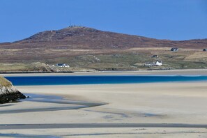 A beach with a clear view of the sea, a sandy shore, and a hill with a structure on top.