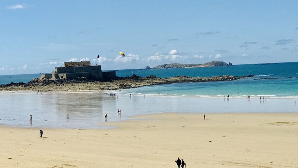 A beach with a large building, calm waters, and clear skies.