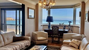 A living room with a view of the sea, a chandelier, and a desk with a lamp.