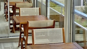 A row of wooden tables and chairs in a modern interior with large glass windows and a view of a building outside.