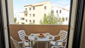 A balcony with a round table and four white plastic chairs. There is a plate with a fruit and a bowl on the table. - Beautiful apartment for 4 people with WIFI, TV, balcony and pets allowed (Saint-pierre-sur-mer)