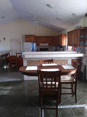 A kitchen with wooden cabinets, a water dispenser, a microwave, and a dining area with a table and chairs.