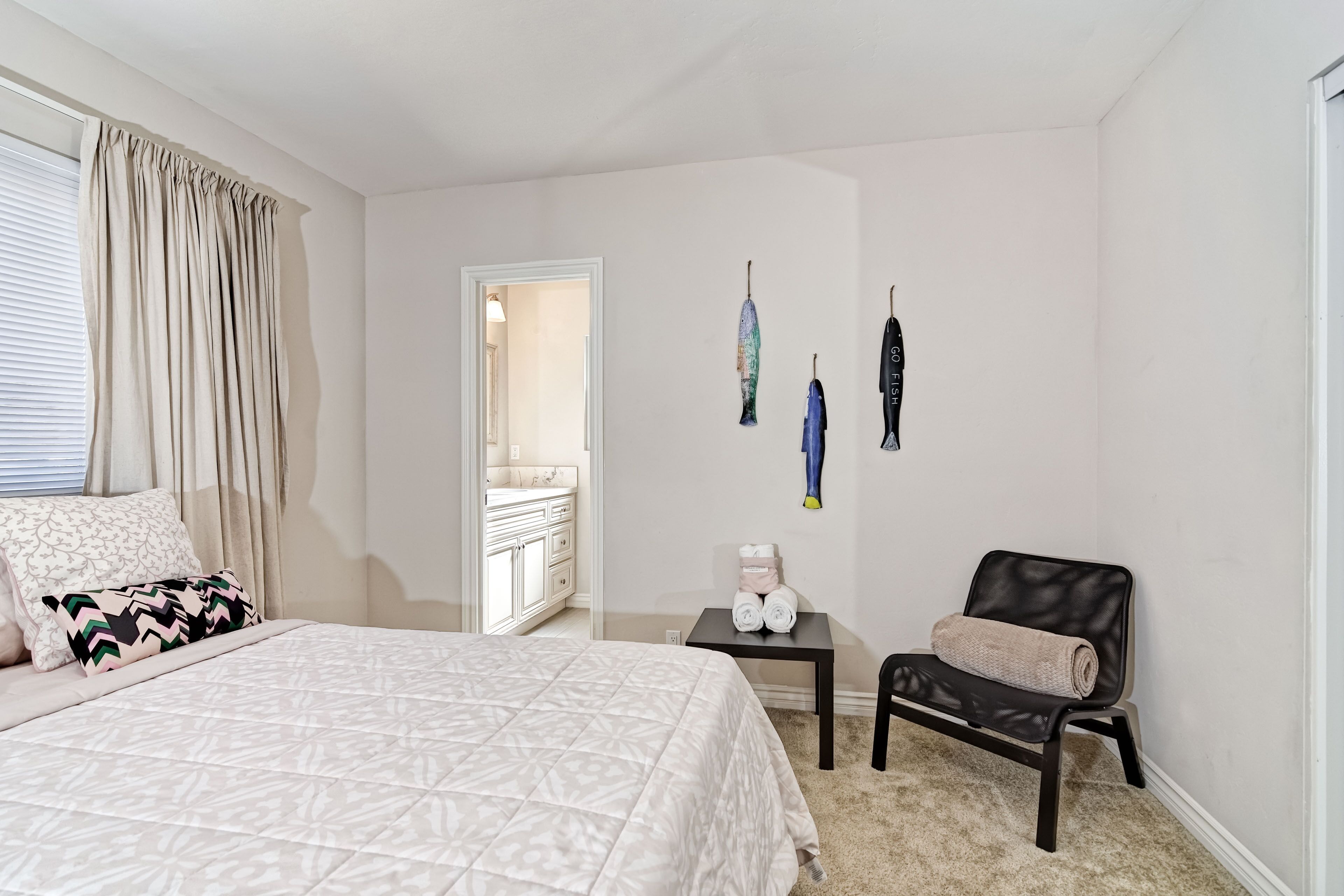 Un dormitorio con cama, una silla, una mesita con toallas y un baño visible a través de una puerta abierta.